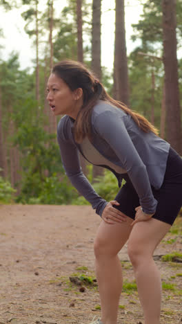 Vertical-Video-Of-Woman-Exercising-Doing-Work-Out-Outdoors-Running-Along-Track-In-Forest-Stopping-For-Breath-Shot-In-Real-Time-2